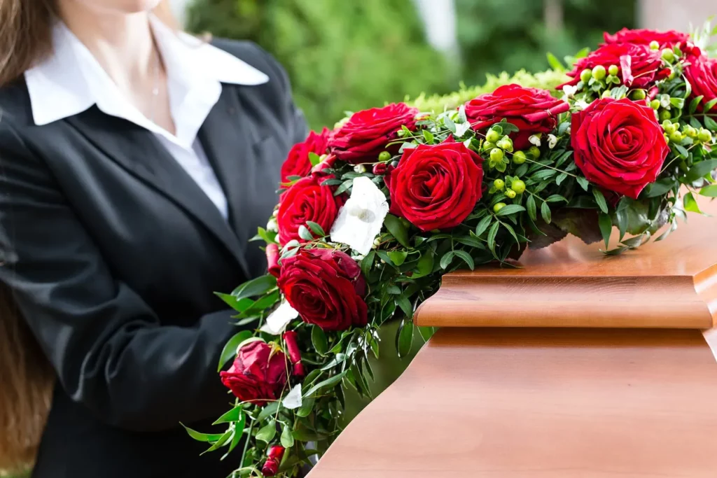 Composition florale de roses rouges disposée sur un cercueil en bois lors d'obsèques.